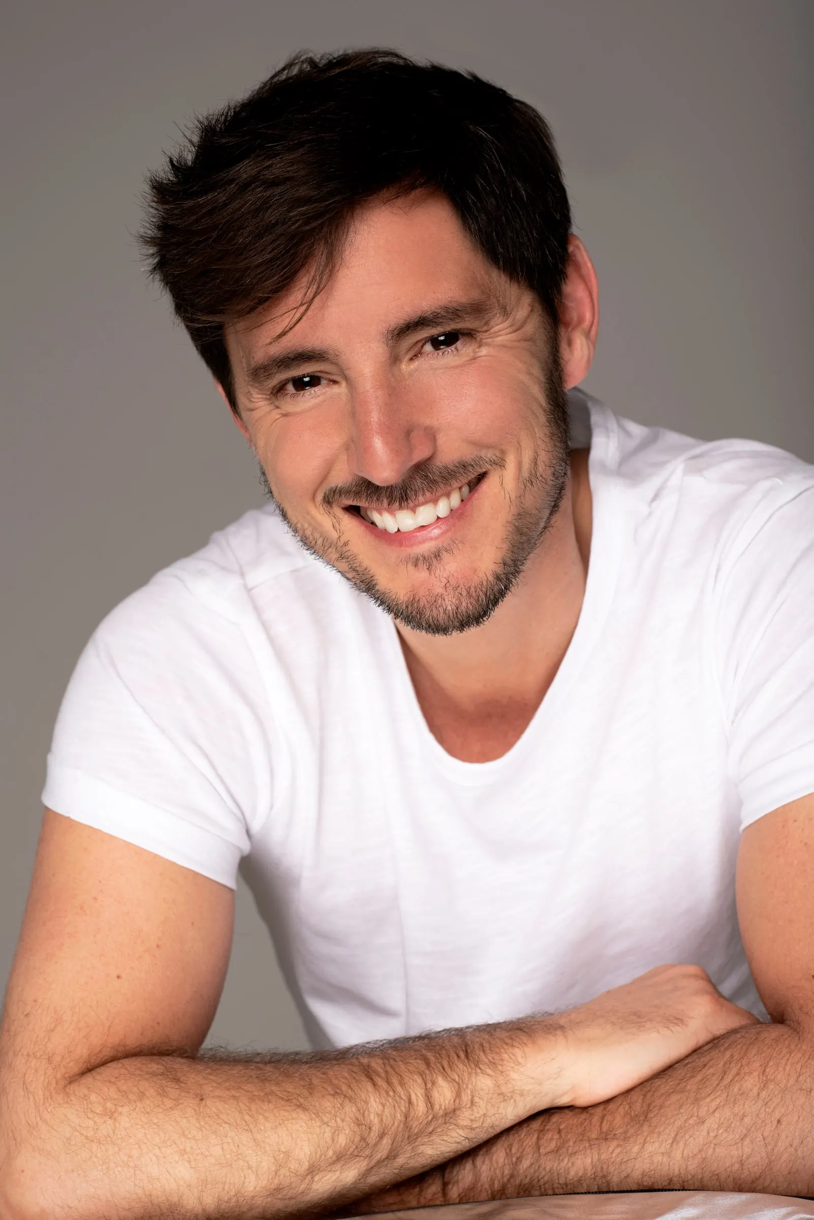 Bernardo Rivera, actor, sonriendo con camiseta blanca y brazos cruzados
